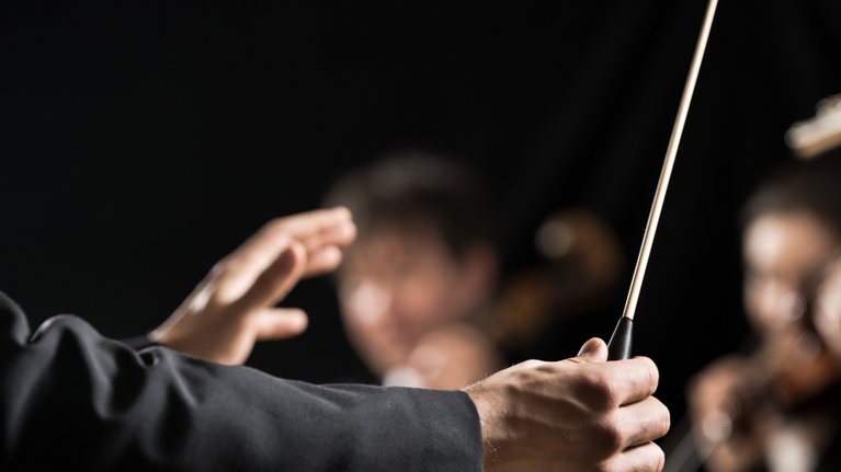 Großaufnahme der Hände eines Dirigenten mit Dirigentenstab