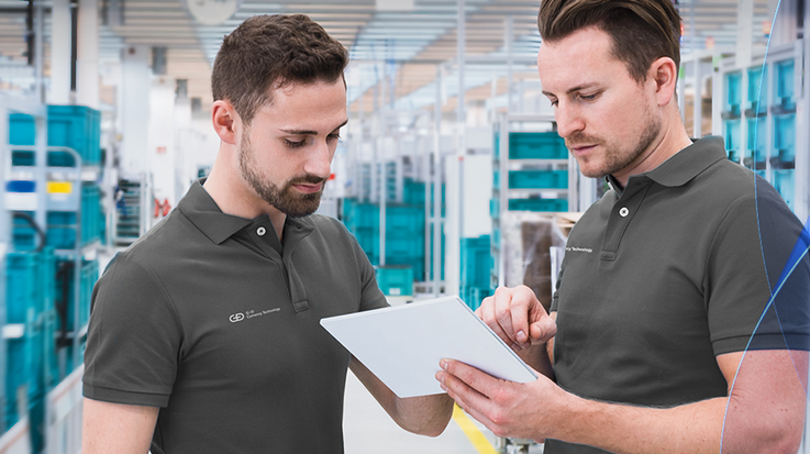 Two G+D employees in polo shirts discuss a clipboard, NotaTrays are in the background