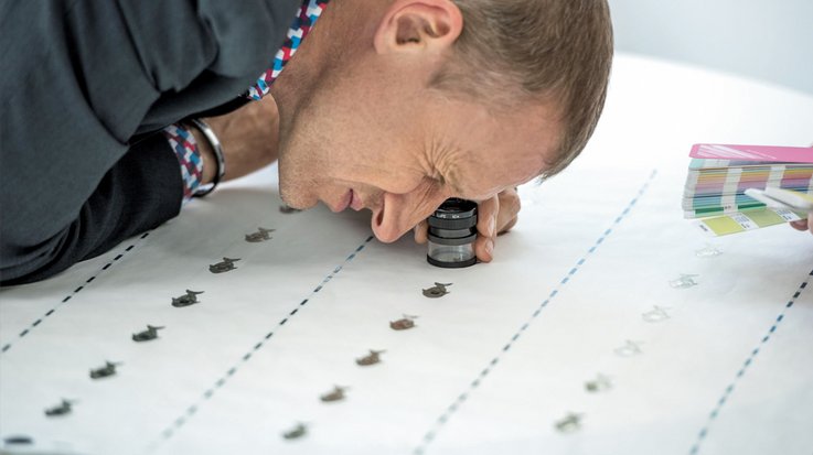 A man looks through a magnifying glass at a small printed sign on a sheet of paper