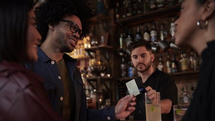 Ein junger Mann bezahlt an einer Bar mit einer Kreditkarte aus Metall