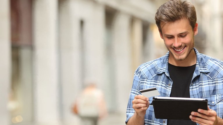 Ein junger Mann hält ein Tablet und eine Kreditkarte in seinen Händen